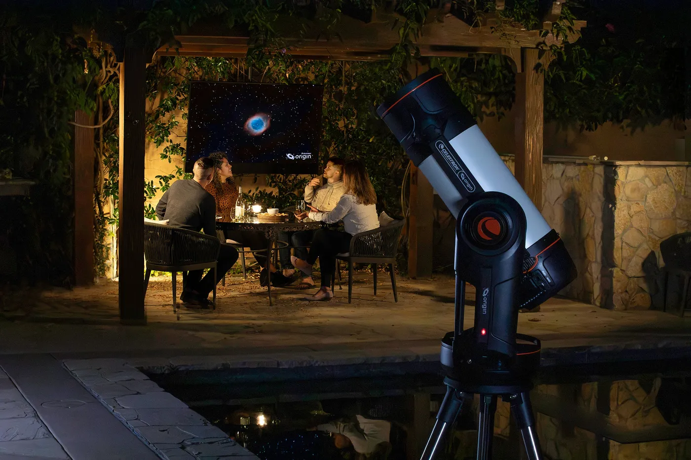 L'Origin dressé au bord d'un bassin sur une terrasse, la nuit. Deux personnes sont attablées devant un écran au fond.