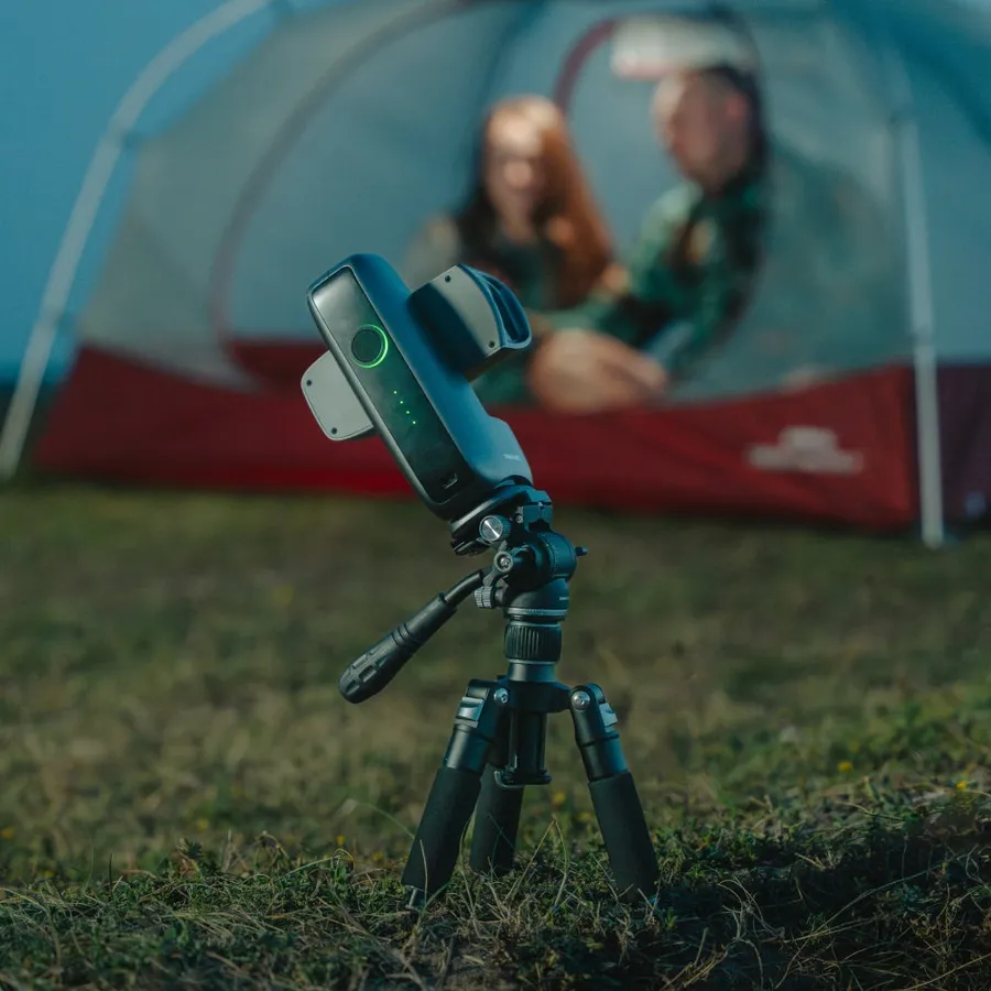 Le DWARF mini sur un trépied photo incliné, planté dans l'herbe devant une tente de camping éclairée.
